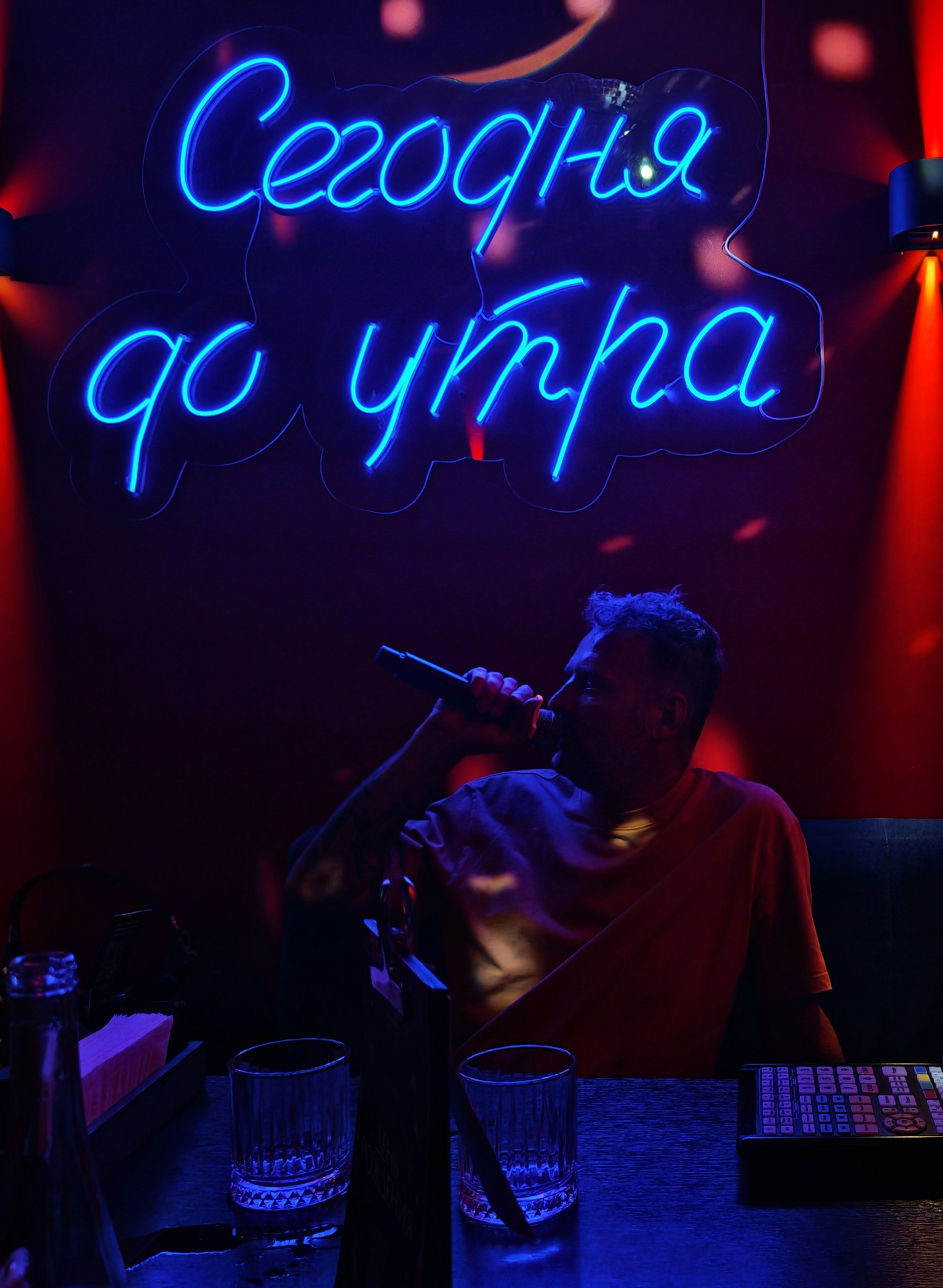 Adult singing karaoke beneath colorful neon lighting